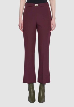 Pantaloni bordeaux con vita aderente, taglio a gamba larga e dettaglio fibbia con logo dorato sulla cintura. Tessuto strutturato; abbinati a stivaletti verde oliva alla caviglia.