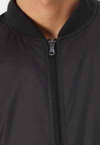 Black bomber jacket with a zippered front, ribbed collar, and smooth texture. The material appears lightweight and breathable.