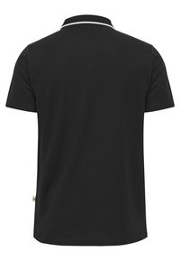 Svart kortärmad pikétröja i bomull med ribbad krage och vit kant. Etikett på den nedre sidan tillför en anmärkningsvärd detalj.