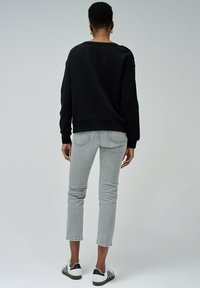 Sweat-shirt noir à coupe décontractée, avec des poignets côtelés, associé à un jean slim gris clair et des baskets noir et blanc. Design simple, sans motifs.