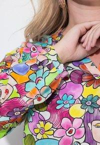 Camicia colorata e a fantasia con motivi floreali nei toni del rosa, blu, verde e arancione. Tessuto traslucido con polsini a bottoni e accenti vivaci.