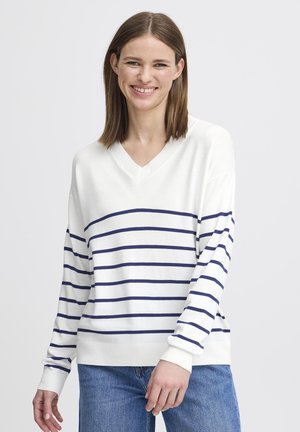 Maglione bianco con righe blu navy, design a V, maniche lunghe, polsini a coste e una vestibilità comoda, abbinato a jeans blu.