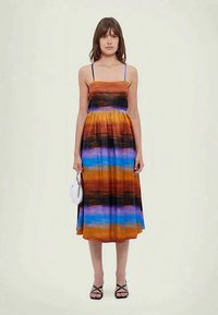 Φόρεμα με πορτοκαλί, μαύρες, μπλε και μωβ ρίγες, αμάνικο σχέδιο, μαζεμένη μέση και μακριά, ροή φούστα. Αξεσουάρ: λευκή τσάντα.