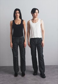 Deux modèles se tiennent côte à côte, portant des débardeurs noirs et blancs avec des pantalons noirs à motifs agrémentés de touches vertes et dorées. Chaussures noires.