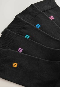 Fem par svarta strumpor med ribbade muddar, försedda med färgglada broderade fyrkantiga logotyper i blått, rosa, teal och orange.