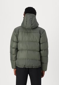 Giacca puffer verde oliva con cappuccio, caratterizzata da sezioni trapuntate e una superficie liscia. Progettata per offrire calore e comfort.