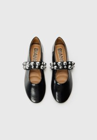 Scarpe in pelle nera con punta arrotondata, dotate di una larga fascetta nera decorata con borchie argentate sulla parte superiore e con solette color nocciola.