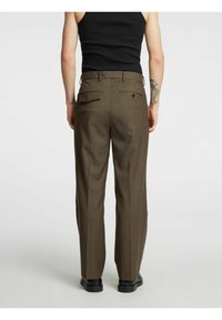 Bruine, op maat gemaakte broek met een vlakke voorkant, achterzakken en een recht model. Voorzien van een subtiel patroon en riemlussen.