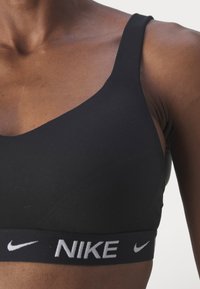Svart sportsbh har et elegant design med brede stropper og et elastisk bånd med logo. Laget av glatt, elastisk stoff.