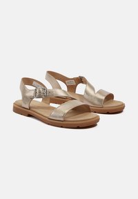 Gyllene metallisk sandaler med korsade remmar och en spänneaccent. Platt sula med en strukturerad yta, designad för komfort och stöd.