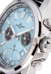 Sidabrinis laikrodis su mėlyna ciferblatu, juodais subdials ir baltais valandų žymekliais. Nerūdijančio plieno korpusas, chronografo funkcijos ir raštuota kronos akcentai.