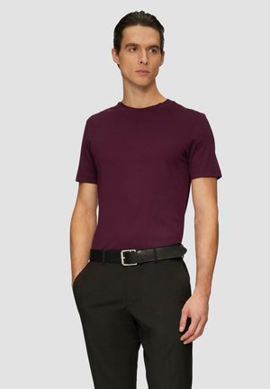 Bordeaux kortgeschouderd T-shirt, ronde hals, gemaakt van katoen. Draag het met een zwarte riem en donkere broeken, staande voor een neutrale achtergrond.