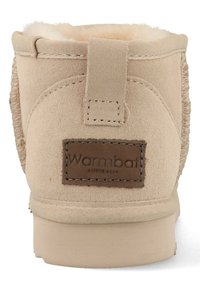Beige suède enkellaars met bontvoering, een versterkte achterlip en een bruine merklabel. Heeft stiksels langs de naden. Platte zool.