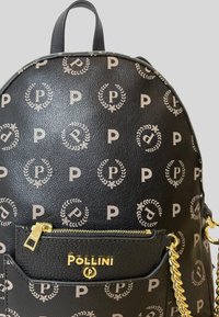 Zaino in pelle nera con motivo ripetuto di logo beige, tasca frontale con zip, hardware dorato e accentuazione a catena. Forma arrotondata con doppio manico.