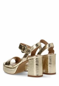 Sandalias de tacón alto metálicas doradas con anchos tacones de bloque, punta abierta, tiras entrelazadas y acentos de hardware circular. Superficie lisa y reflectante.