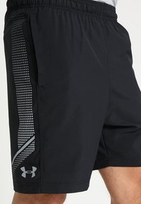 Svarta träningsshorts med elastiskt midjeband och en sidodesign med ett silverrutmönster. Tillverkade av lätt, fukttransporterande material.