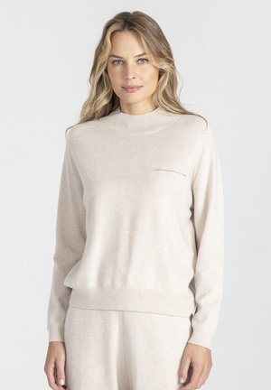 Jasno beżowy sweter z dzianiny o wysokim kołnierzu i długich rękawach. Posiada małą kieszonkę na piersi oraz ściągacze na mankietach i dolnej krawędzi. Miękka faktura.