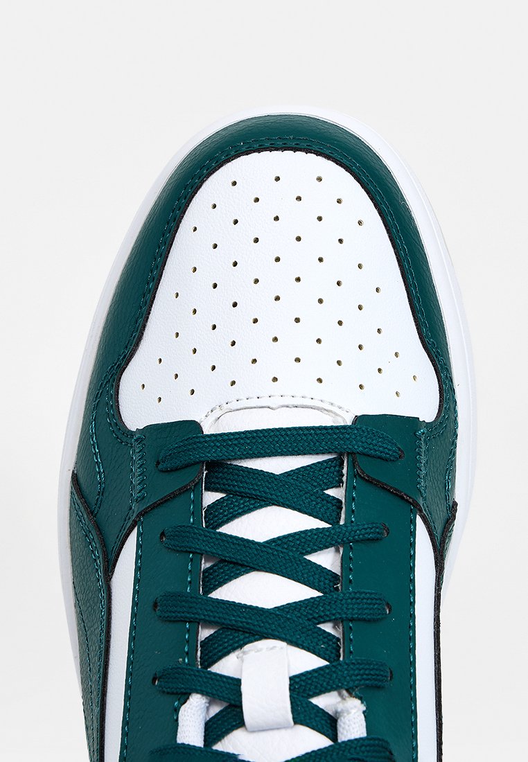 Zapatilla azul verdoso y blanca con puntera perforada, cordones planos azul verdoso, parte superior de cuero, detalles texturizados en los laterales y suela de goma blanca.