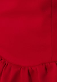Tissu rouge avec une texture lisse et un léger éclat. Présente un volant plissé en bas, créant une silhouette douce et fluide.