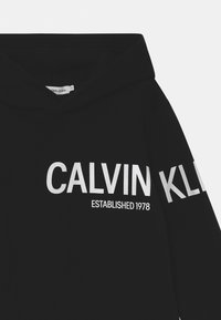 Felpa nera con cappuccio in cotone, caratterizzata da grandi lettere bianche "CALVIN KLEIN" e "ESTABLISHED 1978" sulla parte anteriore.