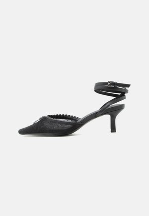 Escarpin noir à bout pointu avec talon kitten, dessus en dentelle, bord festonné et bride autour de la cheville avec fermeture à boucle.