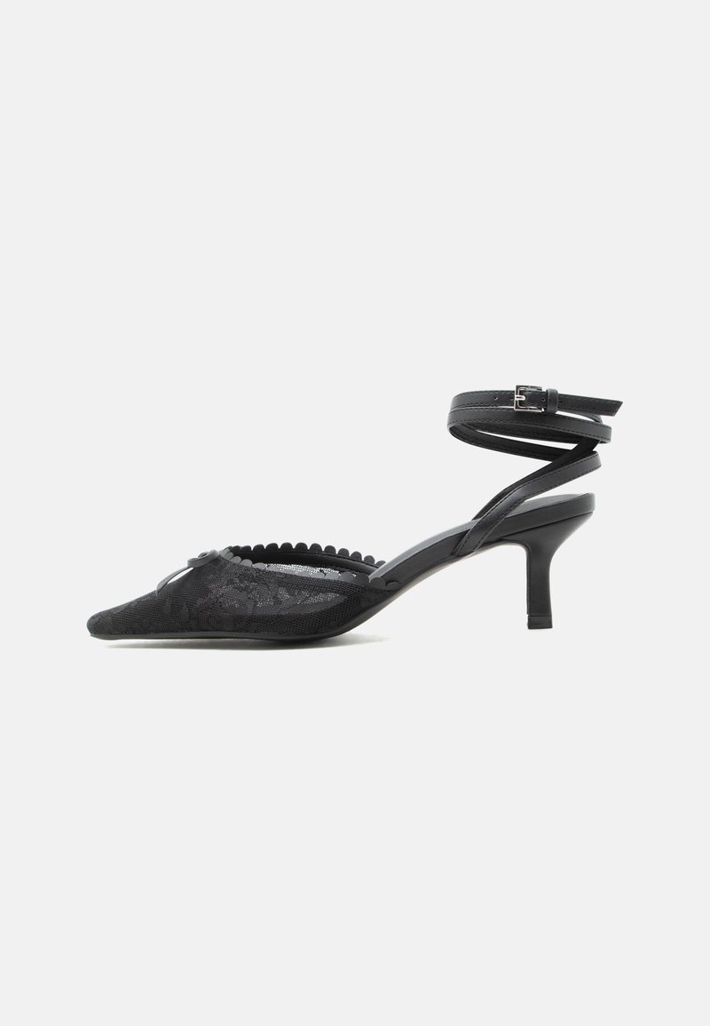 Escarpin noir à bout pointu avec talon kitten, dessus en dentelle, bord festonné et bride autour de la cheville avec fermeture à boucle.