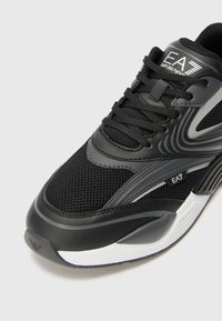 Black athletic shoes with mesh upper, synthetic overlays, and gray accents. Features lace-up closure and cushioned sole. Logo visible on sides.