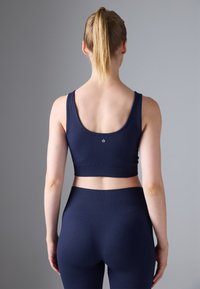 Sutien sport ribbed de culoare bleumarin, cu bretele late și lungime scurtă, având un logo mic pe spate, asortat cu colanți înalți cu talie.