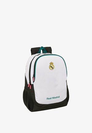 Plecak z białym przodem, czarnymi bokami, logo i napis Real Madrid, dwoma zamykanymi na zamek komorami oraz siateczkowymi kieszeniami po bokach.