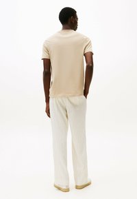 Camiseta de algodón color beige con mangas cortas combinada con pantalones crema de rayas y zapatillas de color claro, vista desde la parte trasera.