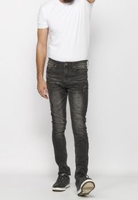 Men's slim-fit jeans in faded black denim, featuring subtle distressing, five pockets, and a classic buttoned closure, paired with black sneakers.