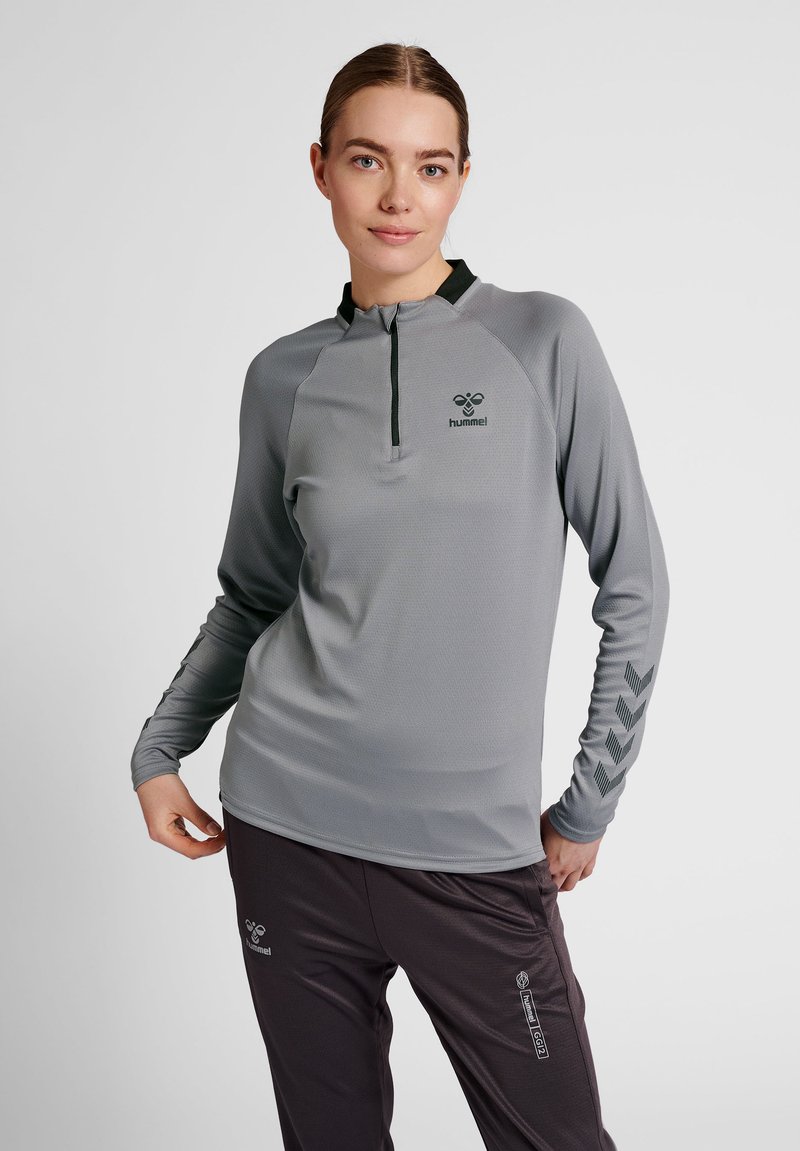 Maglia sportiva grigia a maniche lunghe con colletto a mezza zip, tessuto testurizzato e accenti scuri; presenta un logo e un motivo a zigzag sulle maniche.