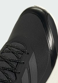 Close-up of a black athletic shoe with textured fabric, black laces, synthetic overlays, and a white cushioned sole.
