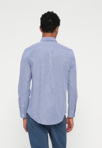 Gestreiftes Hemd mit dünnen blauen und weißen vertikalen Streifen, ausgestattet mit einem klassischen Kragen und abgerundetem Saum, sowie mit Knopfmanschetten.