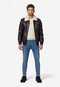 Brun læder bomberjakke med en cremefarvet faux fur krave, parret med en lys sweater og blå jeans. Sorte sneakers fuldender looket.