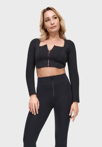 Top corto nero con maniche lunghe, scollo quadrato e zip frontale. Presenta una texture a costine e dettagli con cuciture verticali.