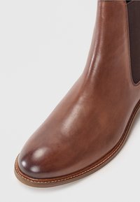 Bota Chelsea de couro castanho com acabamento liso, bico arredondado, painéis laterais elásticos e detalhe de costura contrastante ao longo da sola.