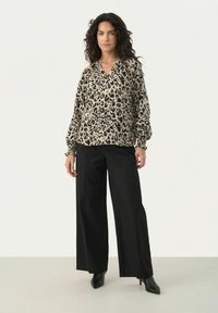 Blouse à imprimé léopard avec des manches ballon, dotée d'un col en V et de poignets smockés. Associée à un pantalon noir à jambes larges et des bottines à talons noirs.