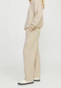 Sudadera beige de gran tamaño y joggers a juego de tela suave. La sudadera tiene puños acanalados y bolsillos. Combinada con zapatillas blancas.