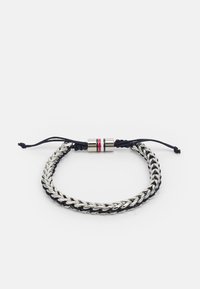 Silverfärgad kedjearmband med ett mörkblått snöre, med ett cylindriskt metallspärr med röda och vita ränder. Justerbar glidslits.