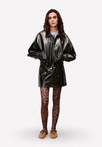 Robe en cuir noir avec un col montant, dot ée d'une fermeture éclair frontale et d'une taille élastique. Associée à des leggings et des chaussures imprimé léopard marron.