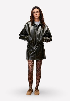 Zwarte leren jurk met hoge kraag, voorzien van een ritssluiting aan de voorkant en een elastische taille. Gecombineerd met bruine legging met luipaardprint en bijpassende schoenen.