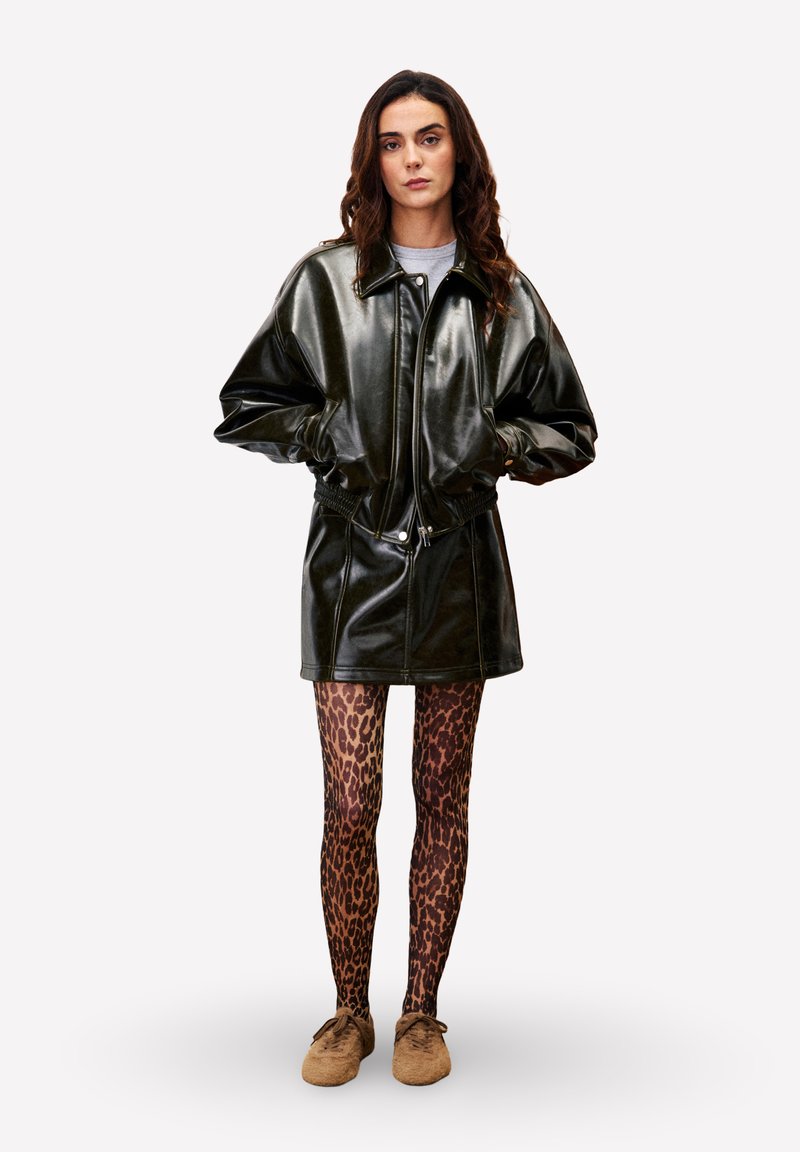 Robe en cuir noir avec un col montant, dotée d'une fermeture éclair frontale et d'une taille élastique. Associée à des leggings et des chaussures imprimé léopard marron.