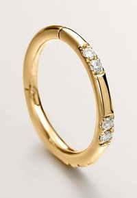 Anillo de oro con un diseño liso y redondeado, con tres piedras preciosas transparentes engastadas en línea, que muestra un acabado pulido y un simple detalle.