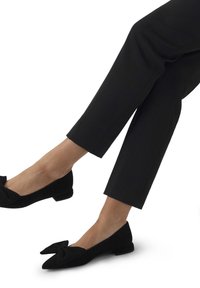 Zwarte suede ballerina's met een strikdetail, puntige neus en een lage hak, gecombineerd met cropped zwarte broeken. Schoon ontwerp met een gladde textuur.