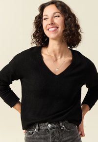 Maglione nero a scollo a V con maniche lunghe, tessuto texturizzato, indossato con jeans grigi a vita alta. Due delicate collane d'oro come accessori.