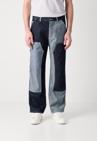 Denim pants with a patchwork design in varying shades of blue. Features contrast stitching, multiple pockets, and a relaxed fit.