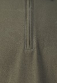 Olivgrön zippered tröja, gjord av texturerad bomull. Har en central dragkedja, förstärkt sömnad och flacka sömmar för hållbarhet.