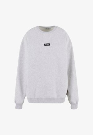 Gaiši pelēks džemperis, kas izgatavots no mīksta auduma, ar garām piedurknēm, ribotām aprocēm un apakšmalu. Uz krūtīm ir neliels melns taisnstūra logotips.