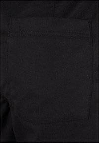 Gros plan d'une poche arrière noire unie sur un pantalon en tissu noir avec des coutures visibles le long des bords.